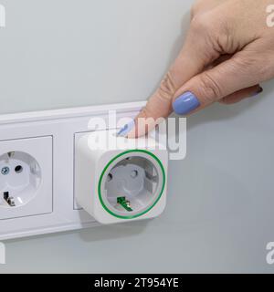 Finger on a wireless extension switch in wall mounted plug Stock Photo