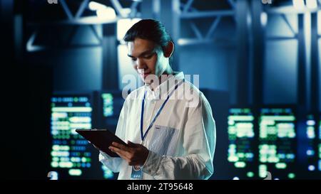 Proactive employee walking through data center electronics providing processing resources for different workloads. Organized engineer evaluating server rigs tasked with solving complex operations Stock Photo