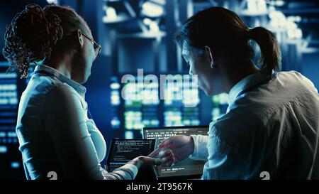 Colleagues programming in server farm housing advanced infrastructure storing massive datasets. Admins running code on laptop to repair data center racks doing complex computational operations Stock Photo