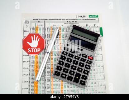 wage slip with marked solidary surcharge, ballpen, calculator and stop sign, abolishment of solidarity surcharge in Germany Stock Photo