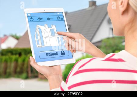 Woman using home security system application on tablet outdoors, closeup Stock Photo