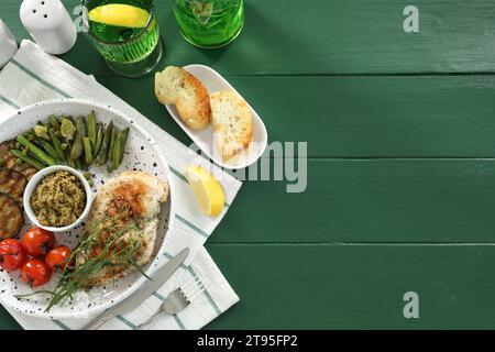 Tasty chicken, vegetables, drink with tarragon and pesto sauce served on green wooden table, flat lay. Space for text Stock Photo