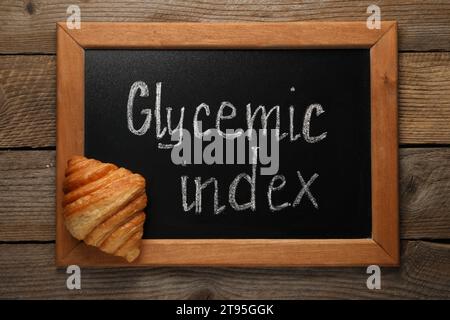 Small chalkboard with words Glycemic Index and croissant on wooden table, top view Stock Photo