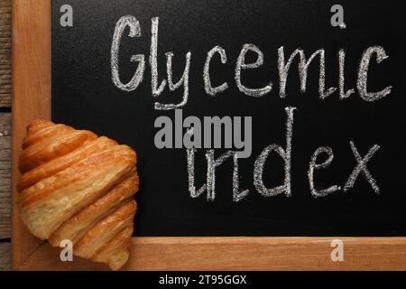 Small chalkboard with words Glycemic Index and croissant on table, top view Stock Photo