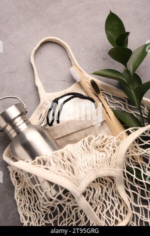 Fishnet bag with different items and green twig on grey table, top view. Conscious consumption Stock Photo