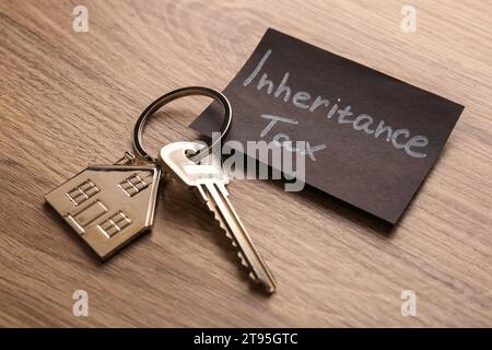 Inheritance Tax. Card and key with key chain in shape of house on wooden table, closeup Stock Photo