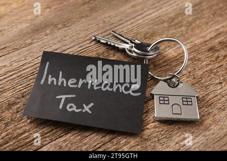 Inheritance Tax. Card and keys with key chain in shape of house on wooden table, closeup Stock Photo