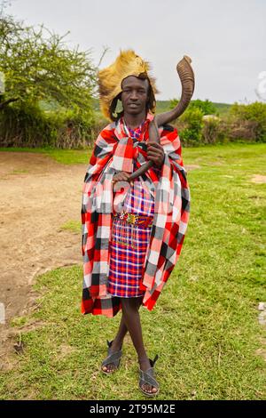 Maasai Mara, Kenya, 25-December-2020 - A Young Maasai Chief and Warrior wearing traditional shuka dress with a lion skin head dress and a kudu horn Stock Photo