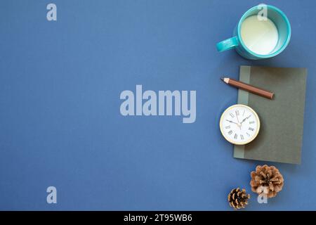 Notebook, clock, colored pencil, cup of milk with pine cone on navy blue background. top view, copy space. workspace Stock Photo