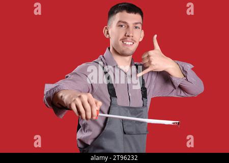 Male builder with tape measure showing 'call me' gesture on red background Stock Photo