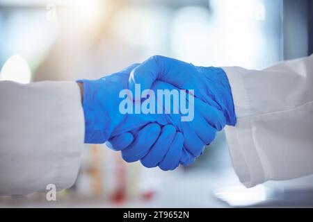 Science, handshake and agreement in laboratory for success, deal or gratitude. Teamwork, medical research and scientist shaking hands in gloves for Stock Photo