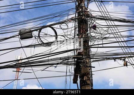 Power line post with tangled electrical wires and capacitors on blue sky with clouds background. Electricity transmission line, power supply Stock Photo