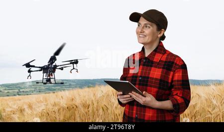 Woman farmer controls drone sprayer with a tablet. Smart farming and precision agriculture.. Stock Photo