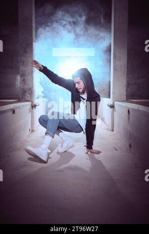 Side view of full body young male in hoodie and jeans preparing performing candle on one hand while practicing breakdance movement in shabby building Stock Photo