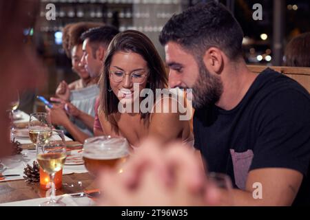 Group of multiethnic coworkers sitting at table in restaurant in evening with drinks and discussing while having fun together Stock Photo