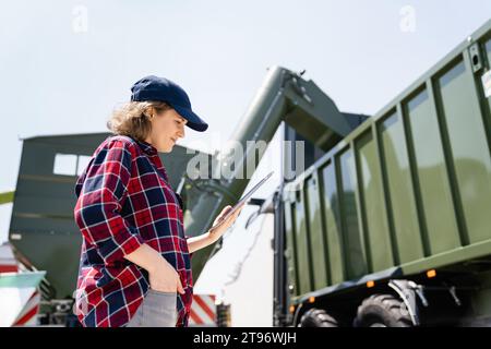 Female farmer with tablet is watching grain loading. Stock Photo