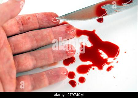 Close-up of arm in bloody puddle and  knife with blood on white surface, concept picture about suicide and murder Stock Photo