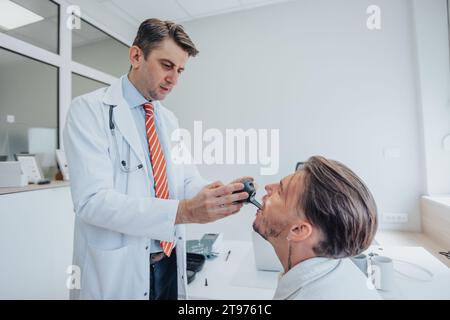 Experienced doctor conducting thorough healthcare examinations in a clinic, checking eyesight, hearing, and throat of young patient. Stock Photo