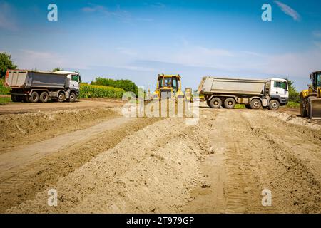 Earthmover with caterpillar is moving earth on the building site parked trucks and another bulldozer are in background. Stock Photo