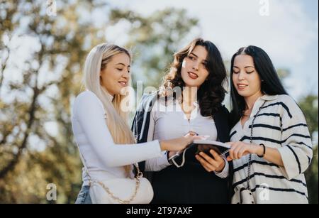 Students collaborate and learn together in a sunny park. They work on a university project, exchanging knowledge and preparing for an exam. Stock Photo