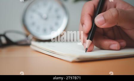Human hands writing notes with pencil on paper on wooden table surface. Stock Photo