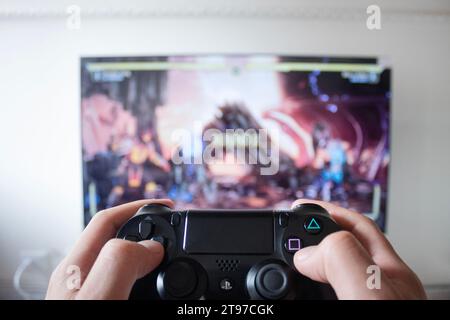 A male hand holding a play station 4 controller with fighter video game in a smart tv at background Stock Photo