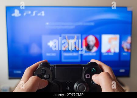 A male hand holding a play station 4 controller with play station 4 interface in a smart tv at background Stock Photo