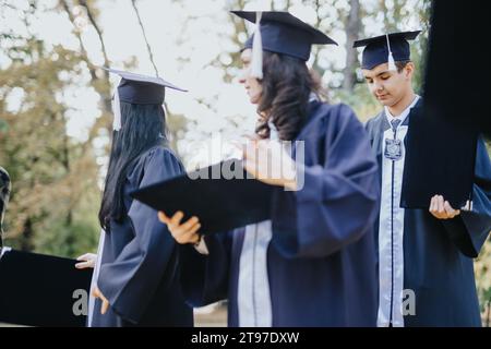 Multiethnic students in graduation gowns celebrate their achievement, chatting happily while walking through a sunny park. Stock Photo