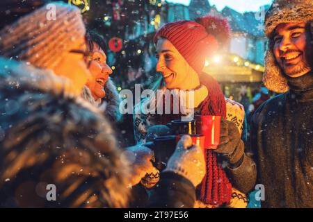 Cheerful friends enjoying mulled wine and hot chocolate in a snowy Christmas market Stock Photo