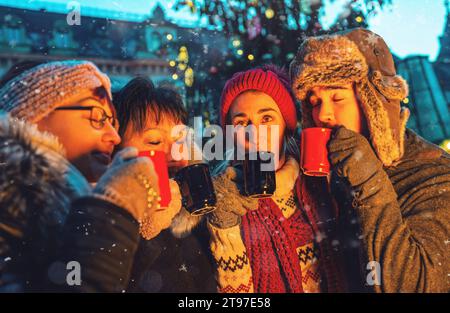 Happy friends having fun drinking mulled wine and hot chocolate at Christmas Marke Stock Photo