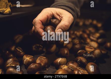 Hand picking roasted chestnuts from a hot tray at a Christmas market Stock Photo