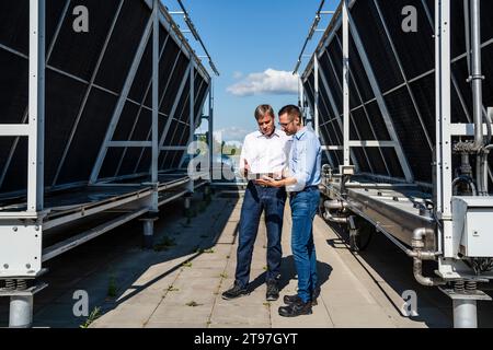 Two businessmen using digital tablet on rooftop beside refrigeration installation Stock Photo