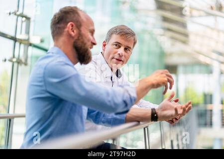 Colleagues discussing innovative business solutions leaning standing in office corridor Stock Photo