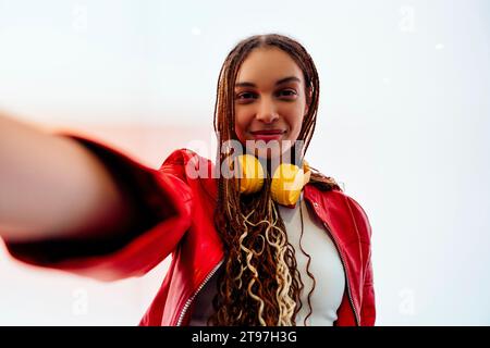 Smiling woman with braided hair taking selfie in front of white wall Stock Photo