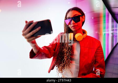 Young woman with sunglasses taking selfie on smart phone in illuminated tunnel Stock Photo