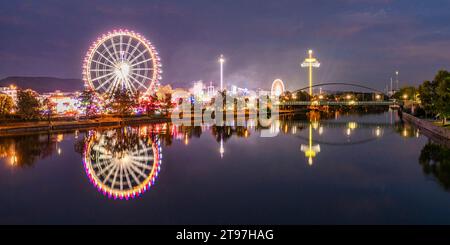 Germany, Baden-Wurttemberg, Stuttgart, Cannstatter Wasen, Panoramic view of glowing Ferris Wheel reflecting in Neckar river at night Stock Photo