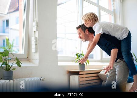 Happy father giving piggyback ride to son at home Stock Photo