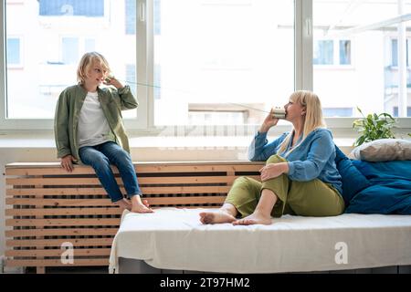Mother talking through tin can phone with son at home Stock Photo