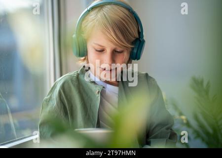 Smiling boy wearing wireless headphones and using tablet PC at home Stock Photo