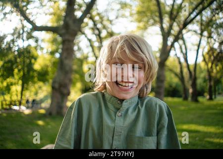 Happy blond boy in front of trees at park Stock Photo