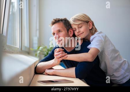 Contemplative father looking through window and holding hands with son at home Stock Photo