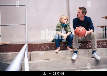 Smiling son sitting with father holding basketball on steps Stock Photo