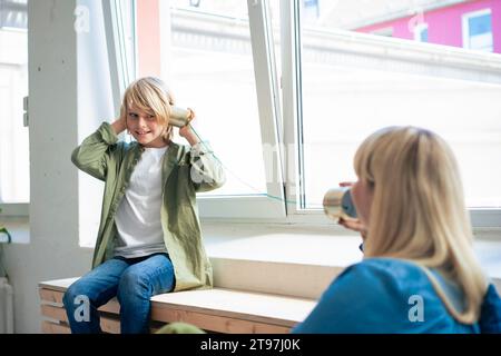 Smiling son talking with mother through tin can phone Stock Photo
