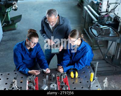 Instructor holding tablet PC teaching trainees using CNC tools at workshop Stock Photo