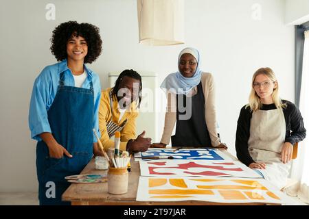 Smiling artists around desk with paintings in studio Stock Photo