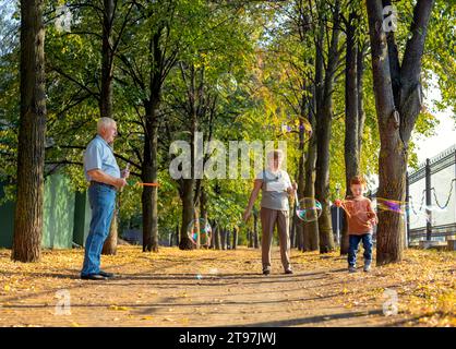 Boy making soap bubbles with grandparents in park on sunny day Stock Photo