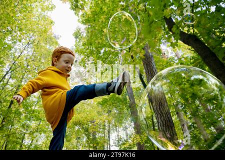 Playful boy kicking soap bubbles in autumn forest Stock Photo