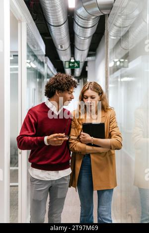 Multiracial business colleagues discussing and walking in corridor at work place Stock Photo