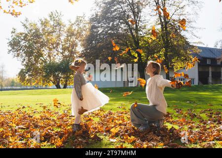 Happy mother and daughter playing with autumn leaves on sunny day Stock Photo