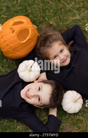 Boy and girl lying on grass near pumpkins at Halloween Stock Photo